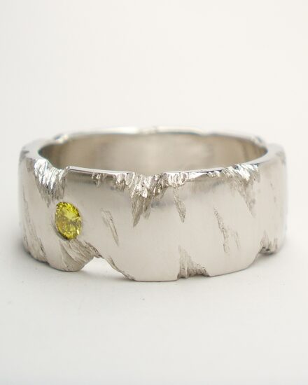 An 8mm broad platinum ring with fractured rock effect and flush set with a 2.8mm HTHP treated canary yellow diamond.