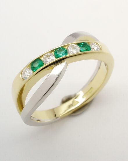 A 7 stone round brilliant cut diamond and emerald cross-over style ring mounted in 18ct. yellow gold and platinum.