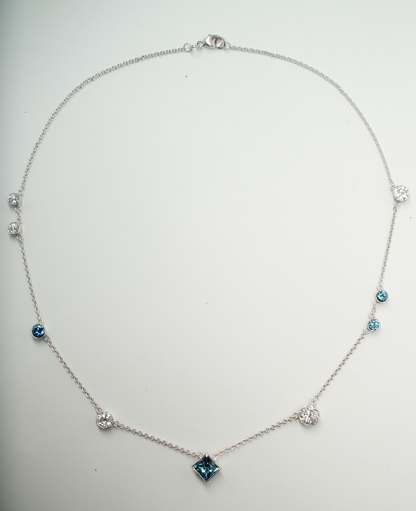A 9 stone ocean blue and white Princess cut and round brilliant cut diamond necklace remodelled from a ring, pendant and pair of earrings.