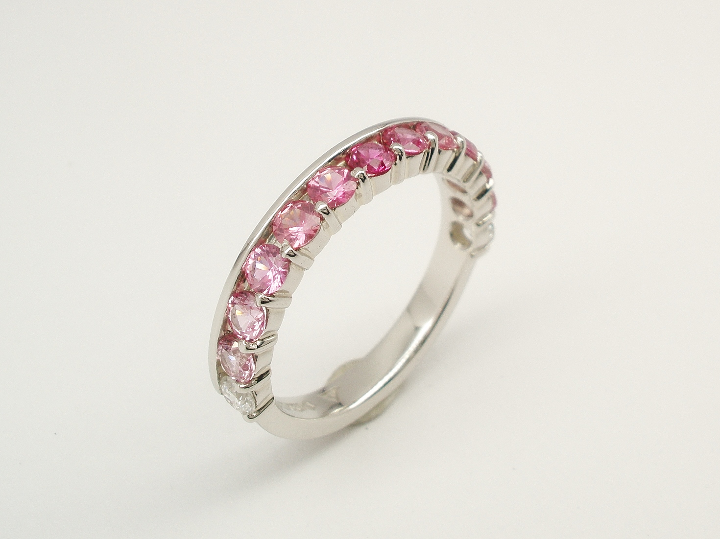 A 13 stone round pink sapphire and brilliant cut diamond ring mounted in platinum. The 11 sapphires graduate in hue from deep colour in the centre to paler around the ring. The sapphires are framed on either side by a single diamond.
