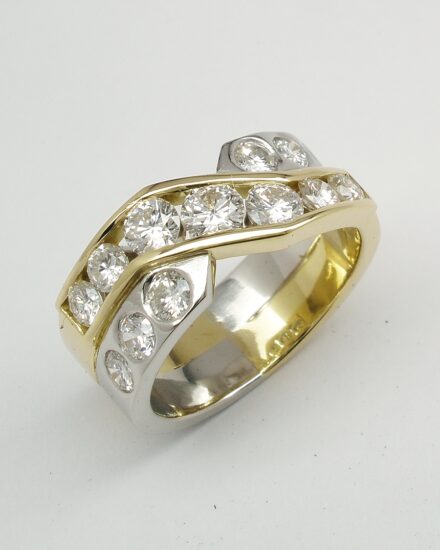 A 13 stone diamond broad cross-over style ring with 7 channel set diamonds and 6 flush set & mounted in 18ct. yellow gold and platinum