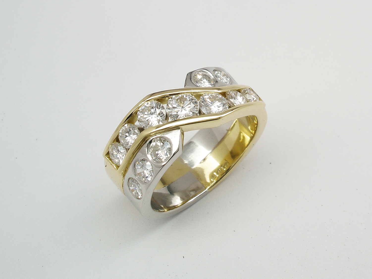 A 13 stone diamond broad cross-over style ring with 7 channel set diamonds and 6 flush set & mounted in 18ct. yellow gold and platinum