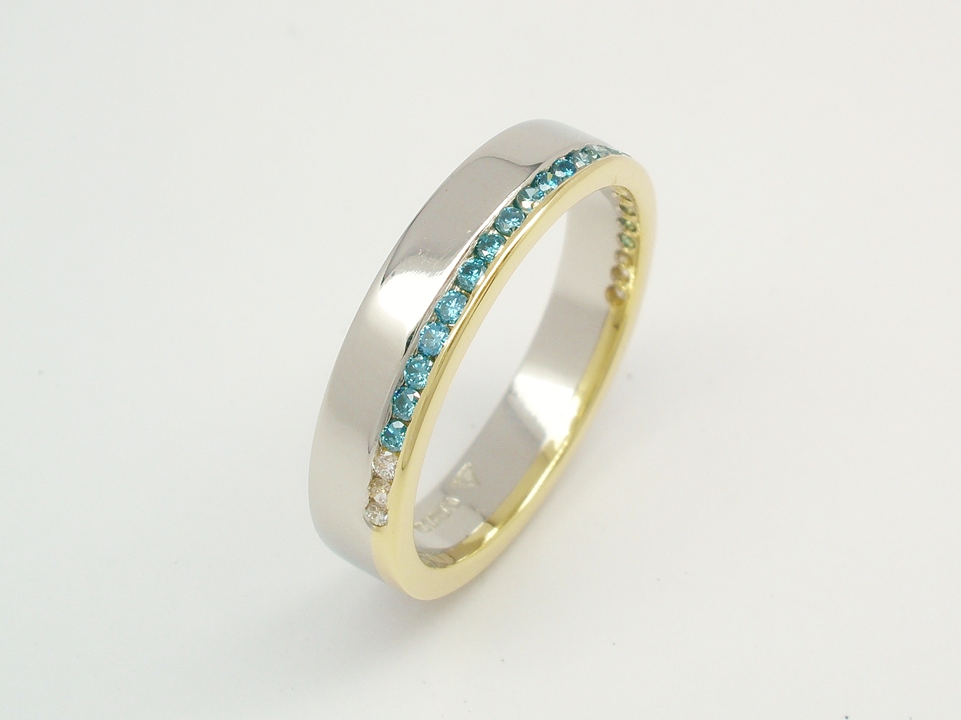A 26 stone Sky Blue and white round brilliant cut diamond offset style wedding ring mounted in platinum and 18ct. yellow gold.