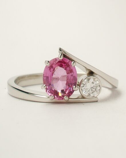A 2 stone oval peg set pink sapphire and rub-over set round brilliant cut diamond straight wishbone cross-over ring mounted in platinum.