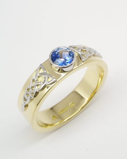 An 18ct. yellow gold single stone round Ceylon sapphire rub-over set in platinum with a fine platinum Celtic motif overlaid on both sides.