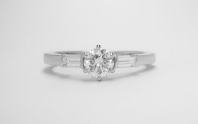 A single stone round brilliant cut diamond ring with baguette shoulders mounted in platinum