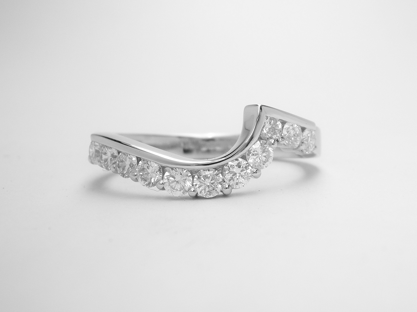An 11 stone round brilliant cut diamond part channel set ring mounted in platinum and shaped to fit around a 2 stone diamond wrap around ring.