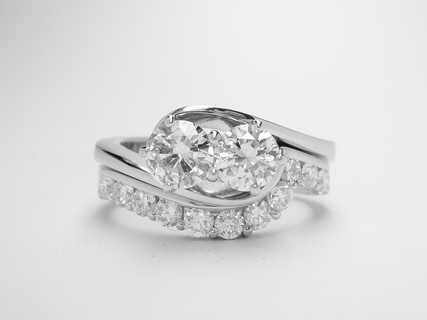 An 11 stone round brilliant cut diamond part channel set ring mounted in platinum and shaped to fit around a 2 stone diamond wrap around ring.
