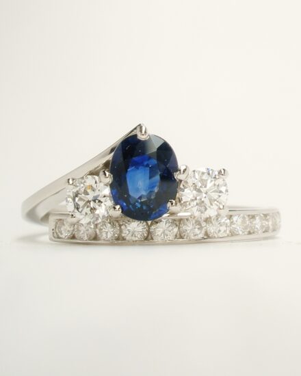 A 3 stone oval sapphire and round brilliant cut diamond straight wishbone cross-over ring with 12 round brilliant cut diamonds channel set in the straight shoulder. This remodelled in platinum from a sapphire and diamond cluster ring and a 2 stone diamond ring.
