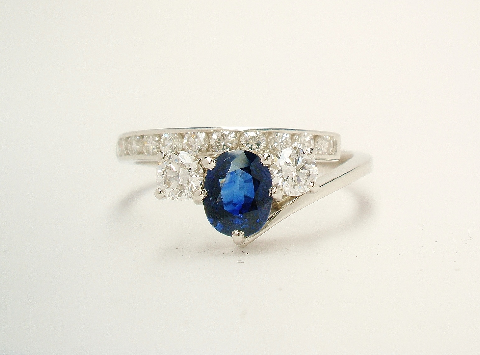 A 3 stone oval sapphire and round brilliant cut diamond straight wishbone cross-over ring with 12 round brilliant cut diamonds channel set in the straight shoulder. This remodelled in platinum from a sapphire and diamond cluster ring and a 2 stone diamond ring.