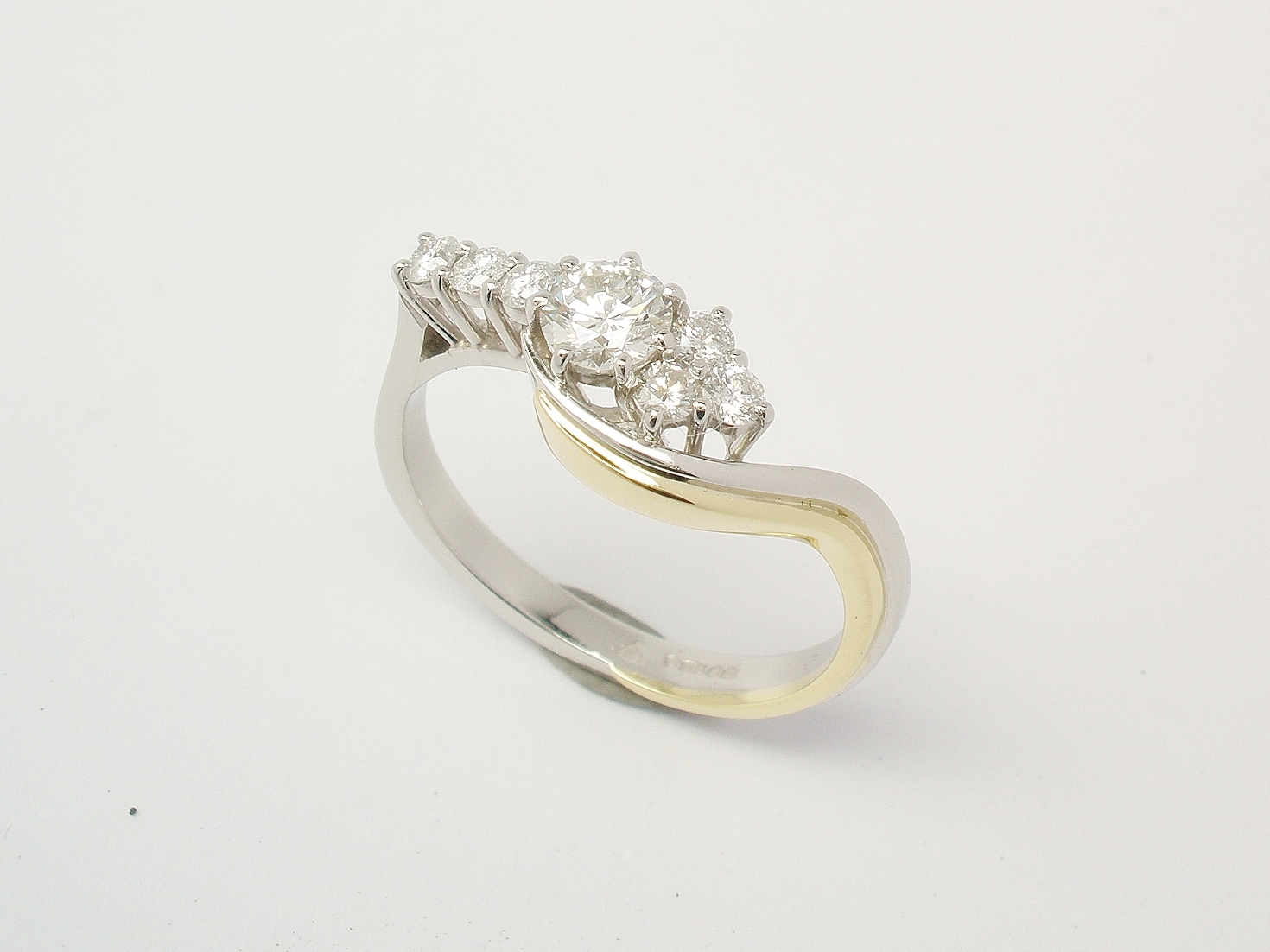 A 7 stone round brilliant cut diamond part cross-over style ring mounted in platinum and edged on one side in 18ct. yellow gold.