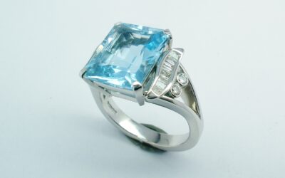 A single stone emerald cut aquamarine ring with baguette diamond panels and small rub-over set round diamonds.