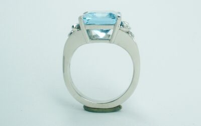 A single stone emerald cut aquamarine ring with baguette diamond panels and small rub-over set round diamonds.