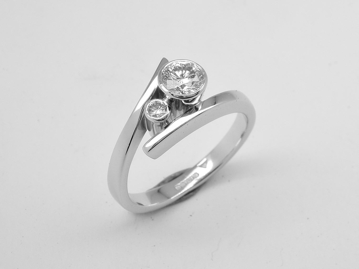 A 2 stone round brilliant cut, rub-over set straight wishbone cross-over style ring mounted in platinum.