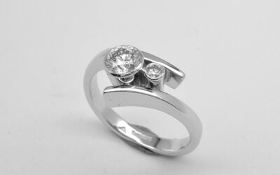 A 2 stone round brilliant cut, rub-over set straight wishbone cross-over style ring mounted in platinum.