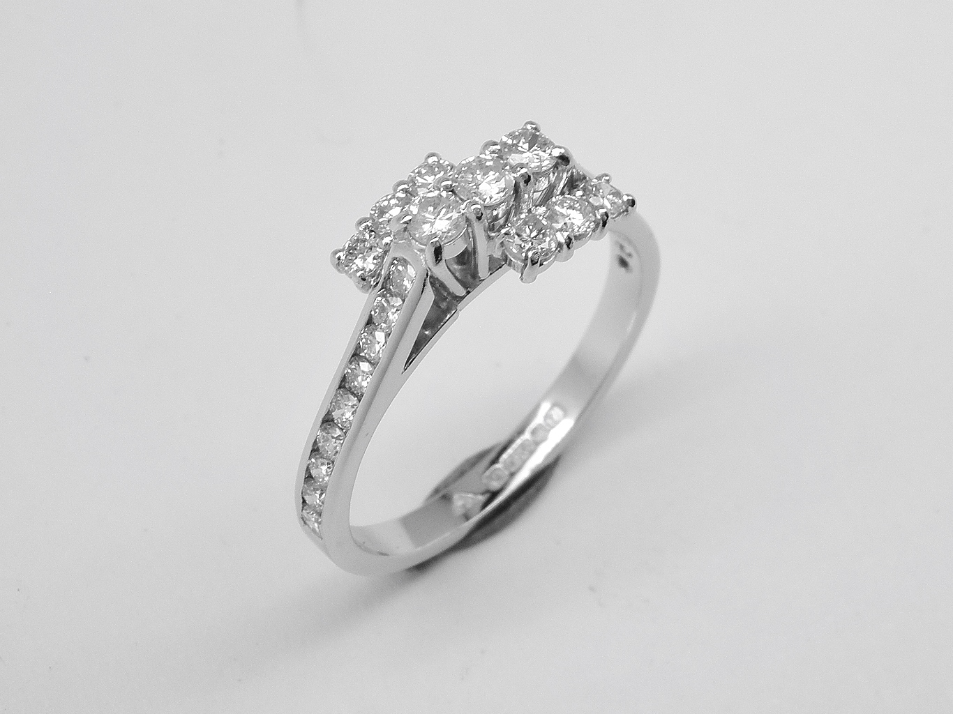 A 9 stone round brilliant cut diamond ring mounted in platinum and channel set with 9 round brilliant cut diamond down each shoulder.