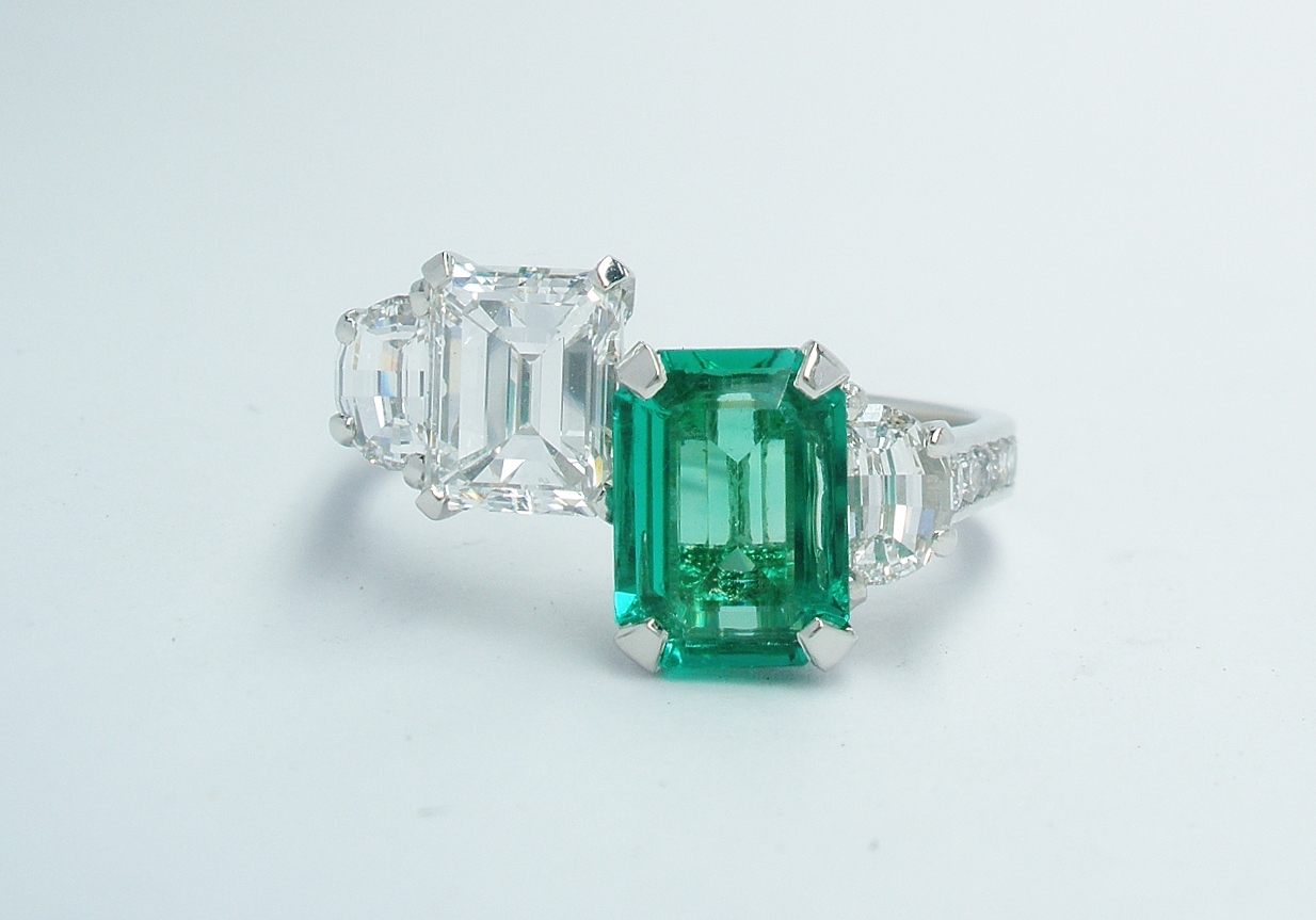 A 4 stone emerald cut emerald, emerald cut diamond and half moon diamonds mounted in platinum with channel set round brilliant cut diamond shoulders.