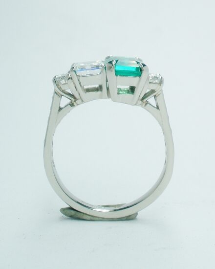 A 4 stone emerald cut emerald, emerald cut diamond and half moon diamonds mounted in platinum with channel set round brilliant cut diamond shoulders.