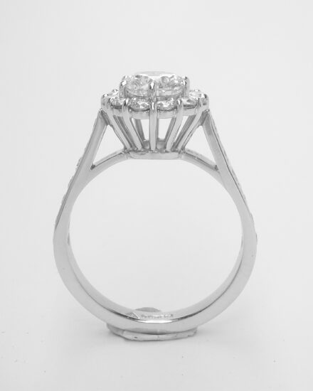A 13 stone round brilliant cut diamond cluster with channel set round brilliant cut diamond shoulders.