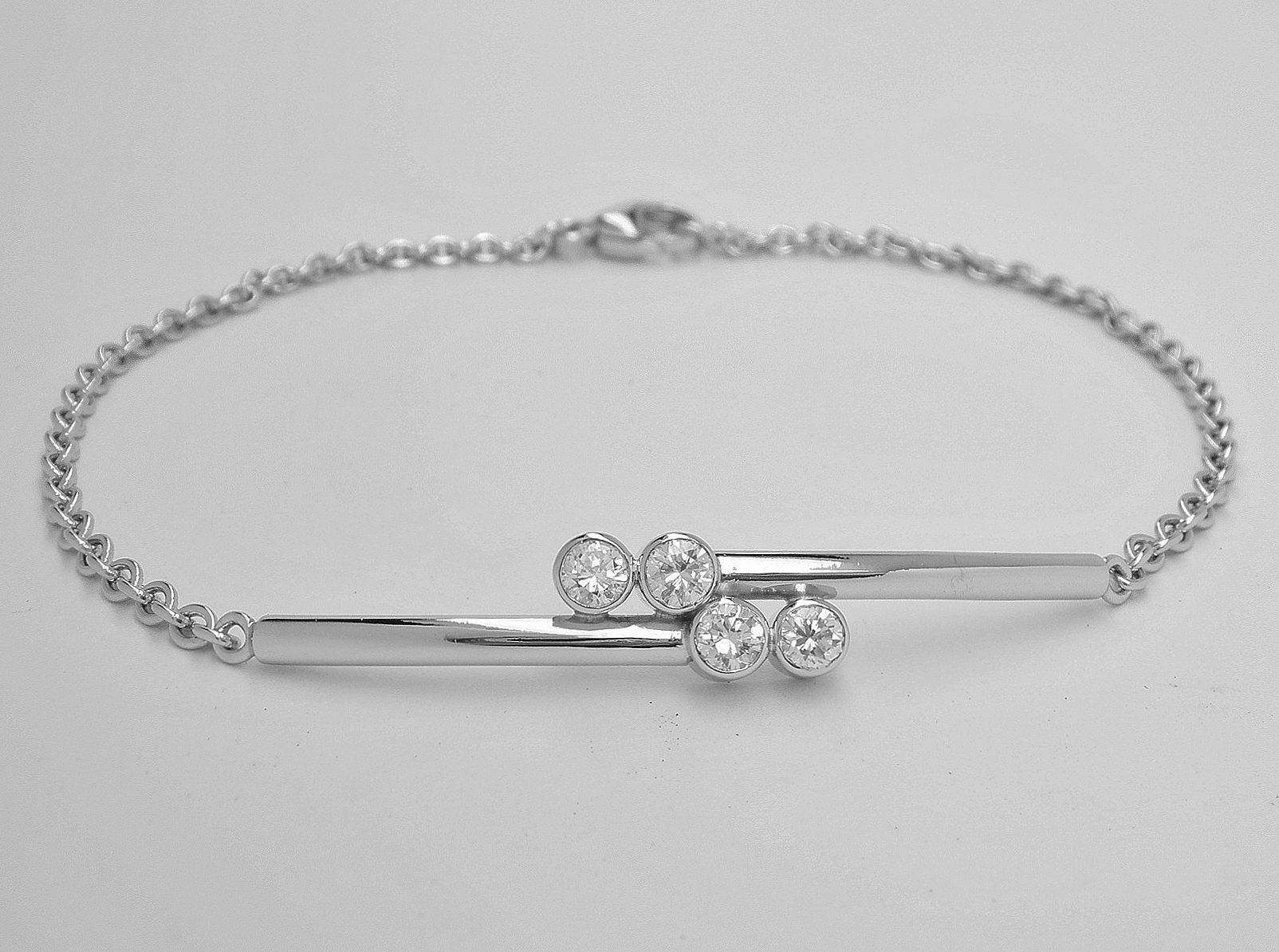A 4 stone rub-over set round brilliant cut diamond cross-over style bracelet with centre solid panel mounted in platinum with platinum chain.