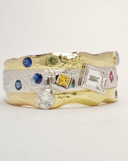 An 11 stone diamond and multi coloured sapphire broad ring mounted in 18ct. yellow gold and platinum.