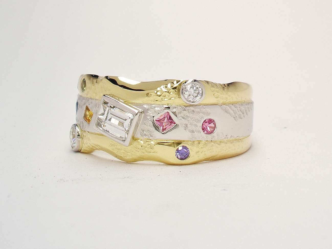 An 11 stone diamond and multi coloured sapphire broad ring mounted in 18ct. yellow gold and platinum.