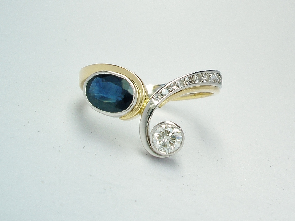 A 2 stone round brilliant cut diamond and oval sapphire curvy wishbone style ring mounted in platinum and 18ct. yellow gold with 12 tapering '8' cut diamonds channel set down one shoulder.