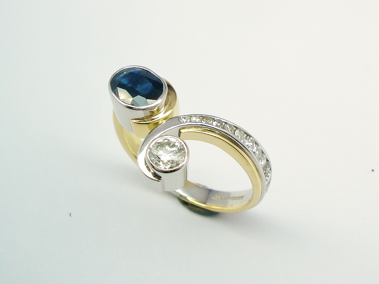 A 2 stone round brilliant cut diamond and oval sapphire curvy wishbone style ring mounted in platinum and 18ct. yellow gold with 12 tapering '8' cut diamonds channel set down one shoulder.