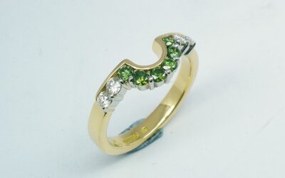 A 10 stone part channel set round brilliant cut green and white diamond wedding ring shaped to fit around a single stone oval diamond engagement ring.