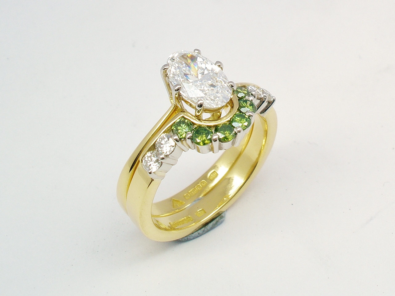 A 10 stone part channel set round brilliant cut green and white diamond wedding ring shaped to fit around a single stone oval diamond engagement ring.
