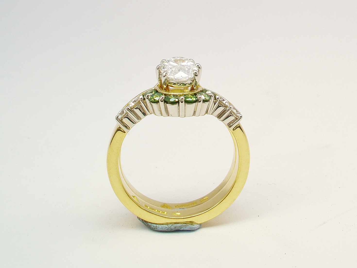 A 10 stone part channel set round brilliant cut green and white diamond wedding ring shaped to fit around a single stone oval diamond engagement ring.