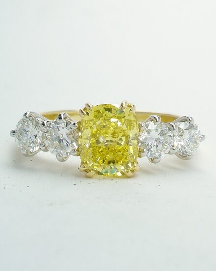 A 5 stone HTHP treated canary yellow cushion shaped diamond and round brilliant cut diamond ring mounted in 18ct yellow gold and platinum.