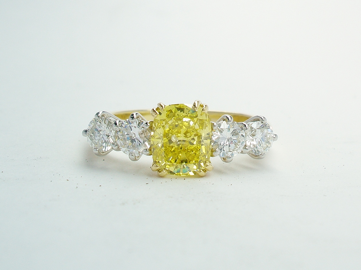A 5 stone HTHP treated canary yellow cushion shaped diamond and round brilliant cut diamond ring mounted in 18ct yellow gold and platinum.