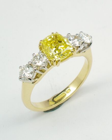 A 5 stone HTHP treated canary yellow cushion shaped diamond and round brilliant cut diamond ring mounted in 18ct yellow gold and platinum.