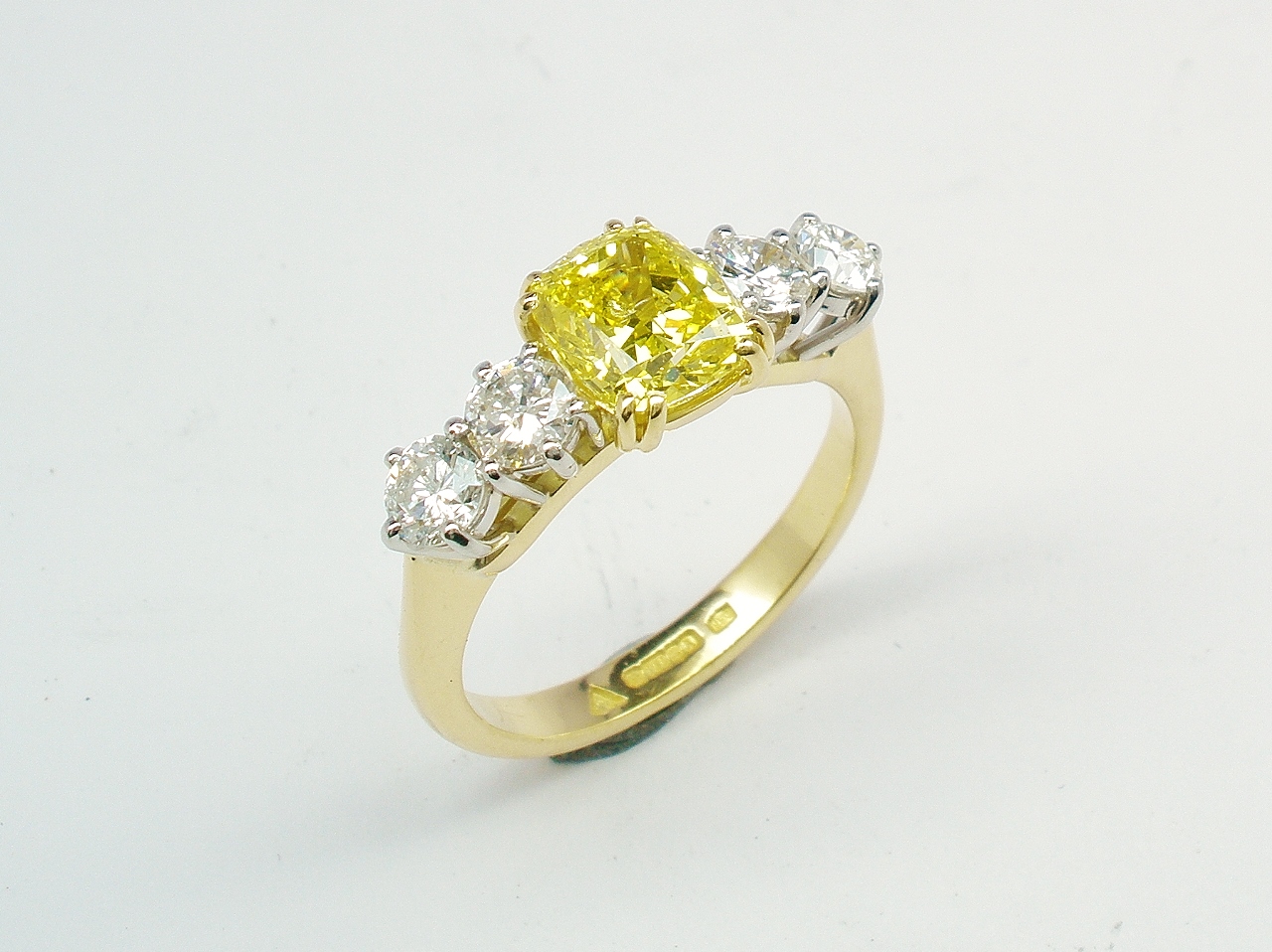 A 5 stone HTHP treated canary yellow cushion shaped diamond and round brilliant cut diamond ring mounted in 18ct yellow gold and platinum.