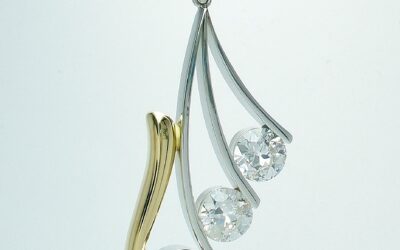 A 3 stone round brilliant cut diamond pendant mounted in platinum and 18ct. yellow gold. The gold takes the form of a 'horn' shape with 3 tapering narrow platinum wires attached.