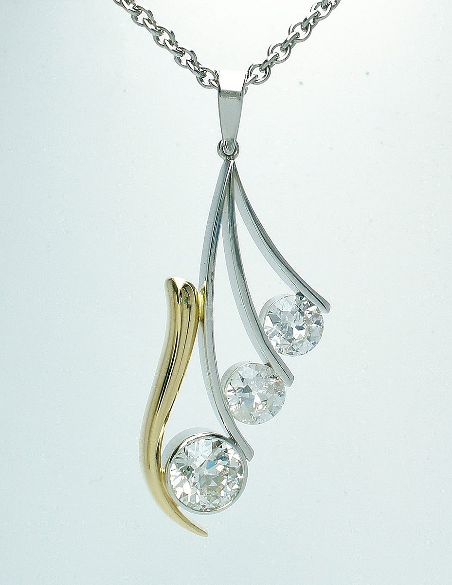 A 3 stone round brilliant cut diamond pendant mounted in platinum and 18ct. yellow gold. The gold takes the form of a 'horn' shape with 3 tapering narrow platinum wires attached.