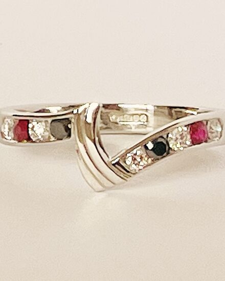 A 9 stone round brilliant cut white diamond, black diamond & ruby ring mounted in platinum and shaped to fit between a 3 stone marquise ruby & diamond ring and 3 stone diamond shaped wedding ring.