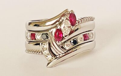 A 9 stone round brilliant cut white diamond, black diamond & ruby ring mounted in platinum and shaped to fit between a 3 stone marquise ruby & diamond ring and 3 stone diamond shaped wedding ring.
