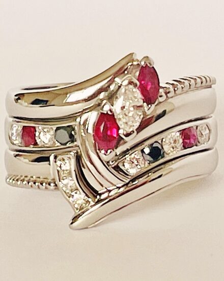 A 9 stone round brilliant cut white diamond, black diamond & ruby ring mounted in platinum and shaped to fit between a 3 stone marquise ruby & diamond ring and 3 stone diamond shaped wedding ring.
