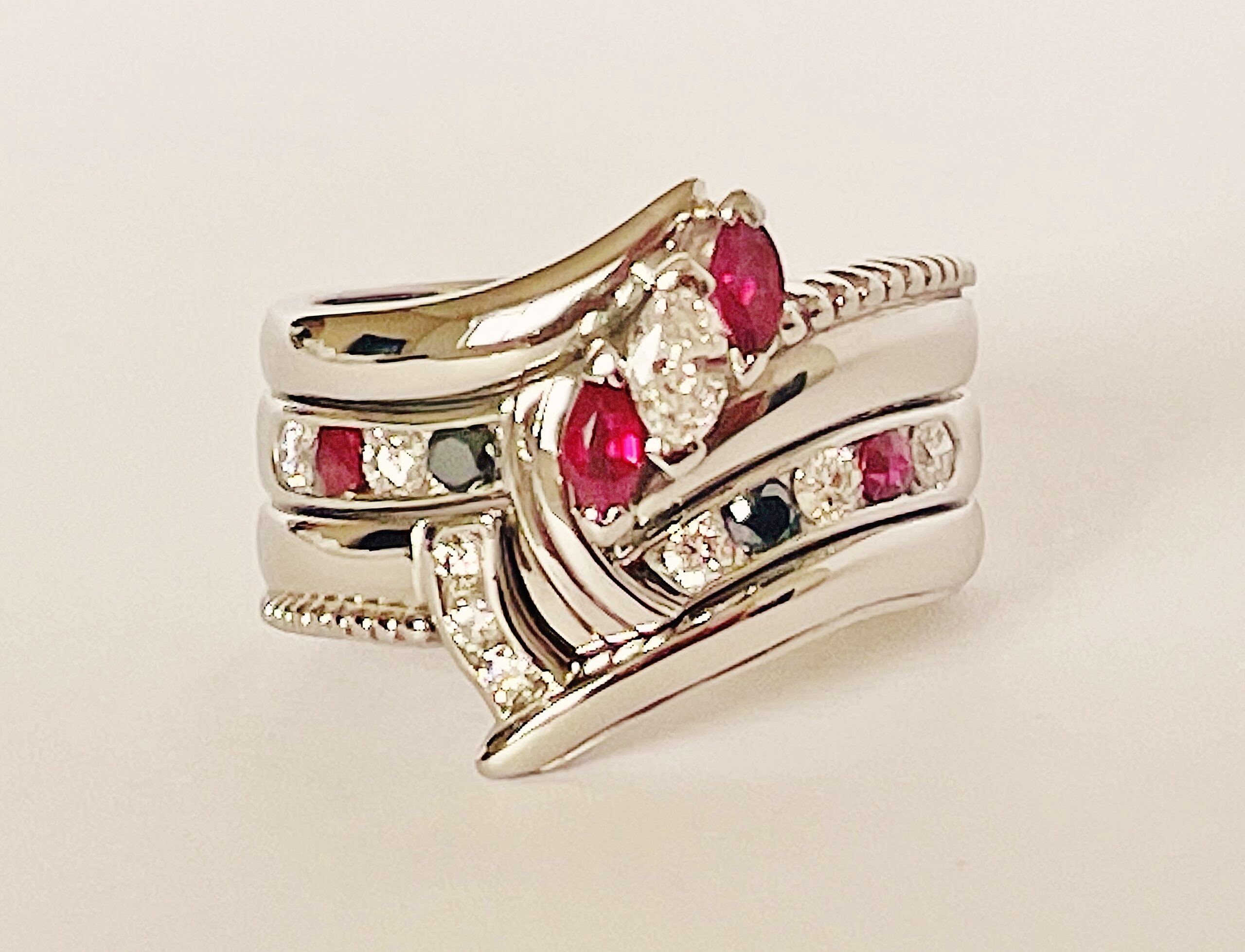 A 9 stone round brilliant cut white diamond, black diamond & ruby ring mounted in platinum and shaped to fit between a 3 stone marquise ruby & diamond ring and 3 stone diamond shaped wedding ring.