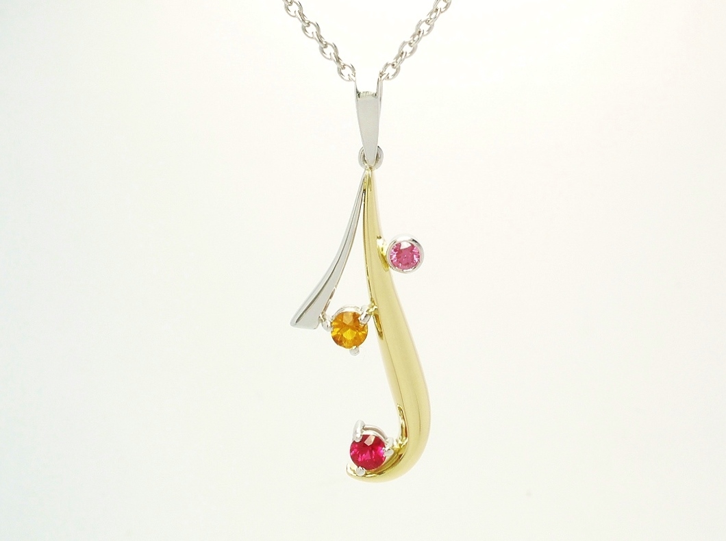 An 18ct yellow gold and platinum pendant loosely designed on an initial 'J' set with a ruby, topaz and purple diamond.